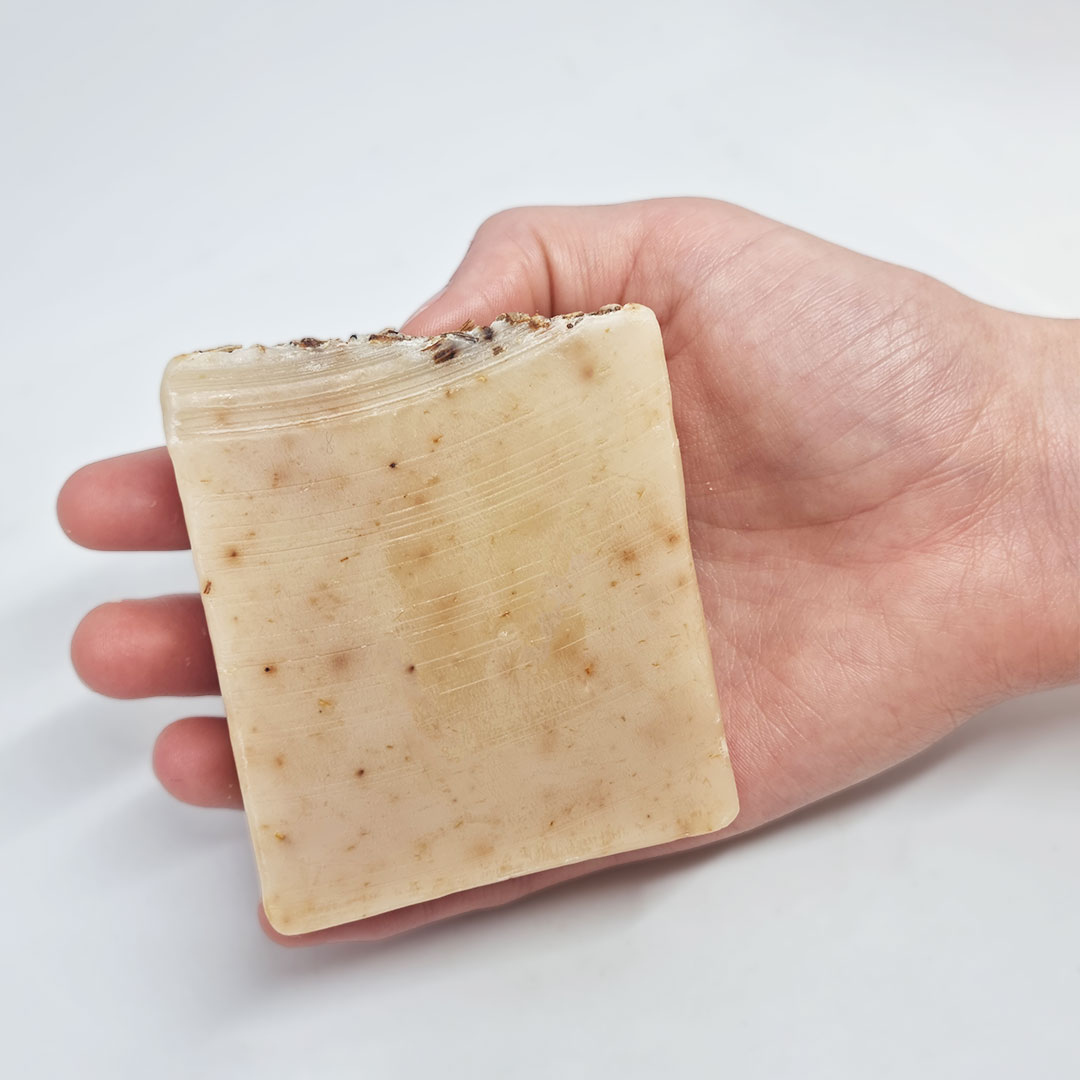 Sabonete de Azeite e Alfazema Sabonete quadrado bege com partículas escuras na mão