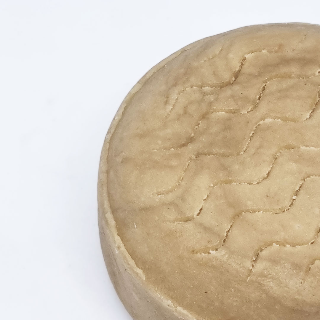 Champô Sólido Cabelo Ondulado - Bambu e Coco Queijo curado redondo com padrão ondulado na superfície