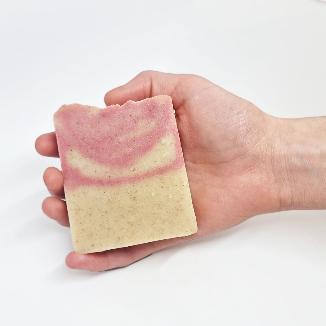 Sabonete de Peónia, Coco e Bergamota Sabonete artesanal retangular creme e rosa numa mão