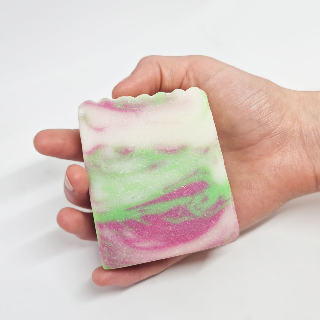 Sabonete de Lírios, Rosas, Jasmim e Seda Sabonete artesanal branco, rosa e verde na mão sobre fundo branco