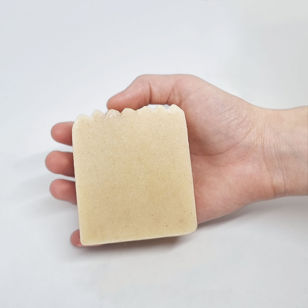 Sabonete de Algas e Amêndoas Sabonete bege com bordas onduladas numa mão