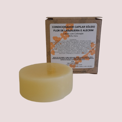 Condicionador capilar sólido redondo amarelo claro junto a embalagem de cartão castanho com texto em português