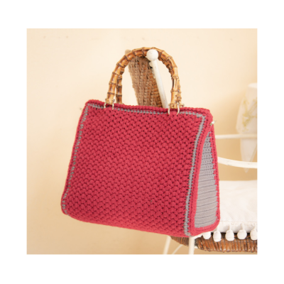 Mala tricotada vermelha com alças de vime pendurada em cadeira branca