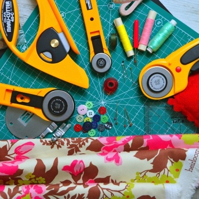 Instrumentos de corte, linhas, botões, almofada de alfinetes e tecido florido sobre base de corte verde