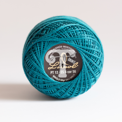 Bola de linha turquesa com etiqueta preta central em fundo branco