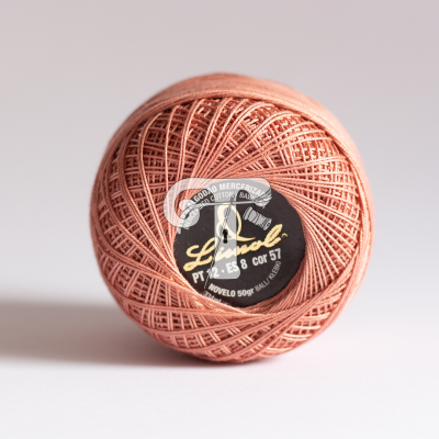 Novelo de linha de algodão mercerizado cor salmão com etiqueta preta sobre fundo branco