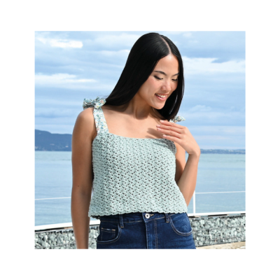Mulher vestindo top azul claro de malha com laços nos ombros junto ao mar