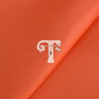 Tecido laranja com ornamento em forma de letra T e agulha de costura