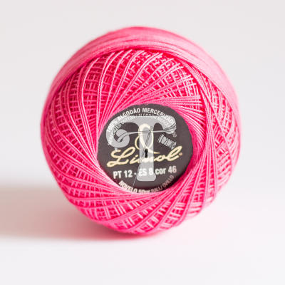 Novelo de linha de algodão rosa com etiqueta preta no centro sobre fundo branco