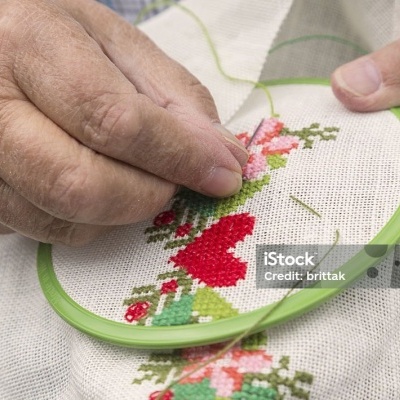 Pessoa bordando tecido branco com floral vermelho e rosa numa moldura verde