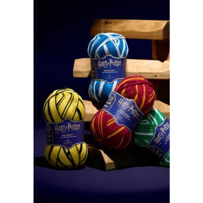 Novel da lã colorida com etiquetas Harry Potter e nomes das casas em fundo azul escuro