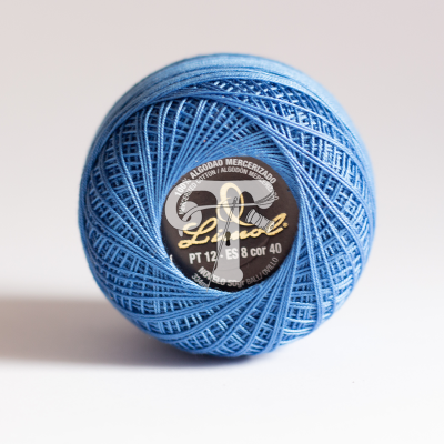 Rolo de linha azul em algodão mercerizado com etiqueta preta e dourada.