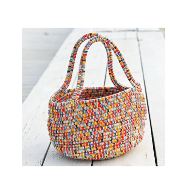 Cesto trançado multicolorido com alças duplas sobre chão de madeira branco