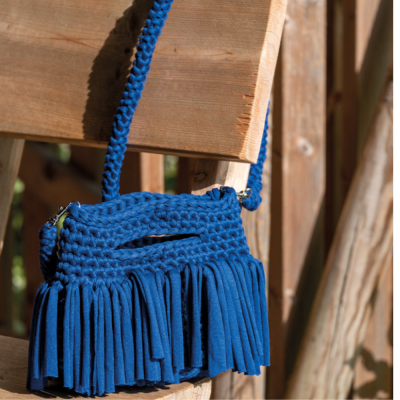 Mala azul de tecido trançado com franjas pendurada numa cadeira de madeira