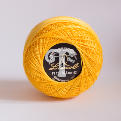 Novelo de linha amarela com etiqueta preta e texto branco e dourado