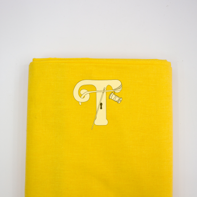 Tecido amarelo com ilustração da letra T com agulha e linha