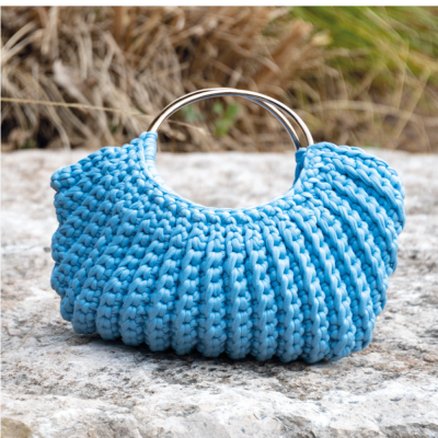 Mala de mão azul tricotada com alças metálicas douradas em superfície rochosa