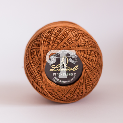 Novelo de linha castanha com etiqueta preta e branca, em superfície branca