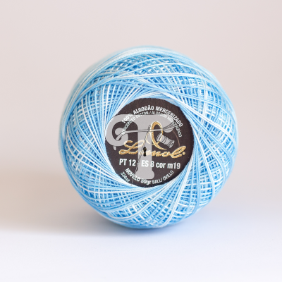 Rolo de linha azul claro em algodão mercerizado com etiqueta preta e branca.