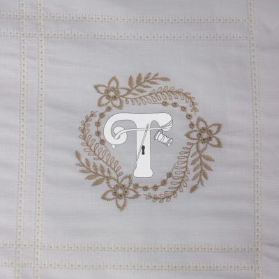 Tecido branco bordado com letra T e flores em tons castanhos