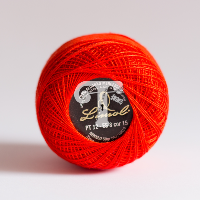 Novelo de linha vermelho com etiqueta preta e branca sobre superfície branca