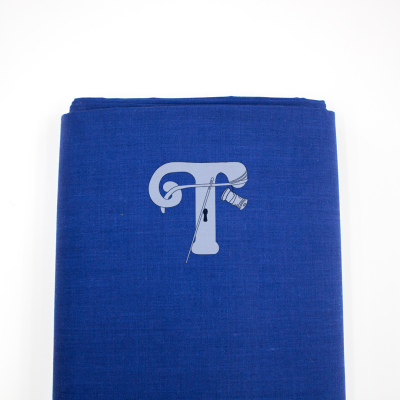 tecido azul com letra T branca, agulha e carretel de linha