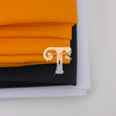 Três tecidos dobrados em cores laranja, preto e branco sobre fundo claro