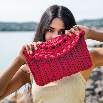 Mala envelope croché vermelha segurada por mulher perto de água