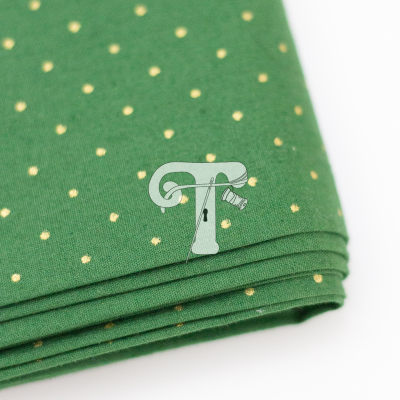 Tecido verde com bolinhas douradas dobrado sobre fundo branco