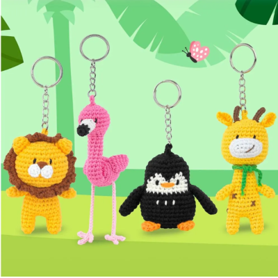 Porta-chaves em crochet de animais (leão, flamingo, pinguim, girafa) em fundo verde com folhas e borboleta.