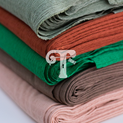 Tecidos enrugados coloridos dobrados em pilha sobre fundo branco.