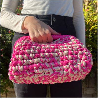 Mala de mão trançada rosa e bege, tecido grosso, ao ar livre.
