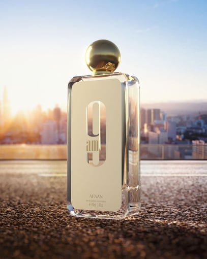 Frasco de perfume dourado com tampa esférica numa superfície urbana ao pôr do sol