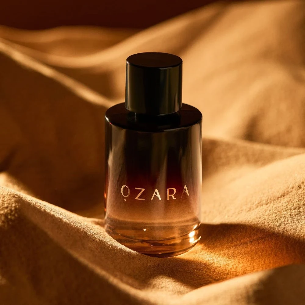 Frasco de perfume OZARA em vidro gradiente castanho sobre tecido dourado.