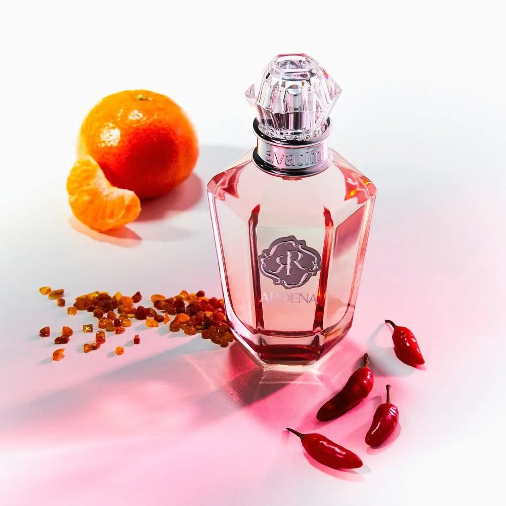 Frasco de perfume de vidro transparente com líquido cor de rosa junto a pimenta vermelha, grãos âmbar e tangerina descascada