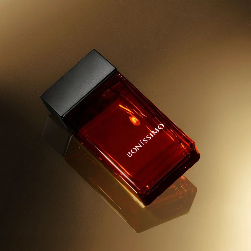 Frasco de perfume vermelho BONISSIMO com tampa preta sobre superfície dourada