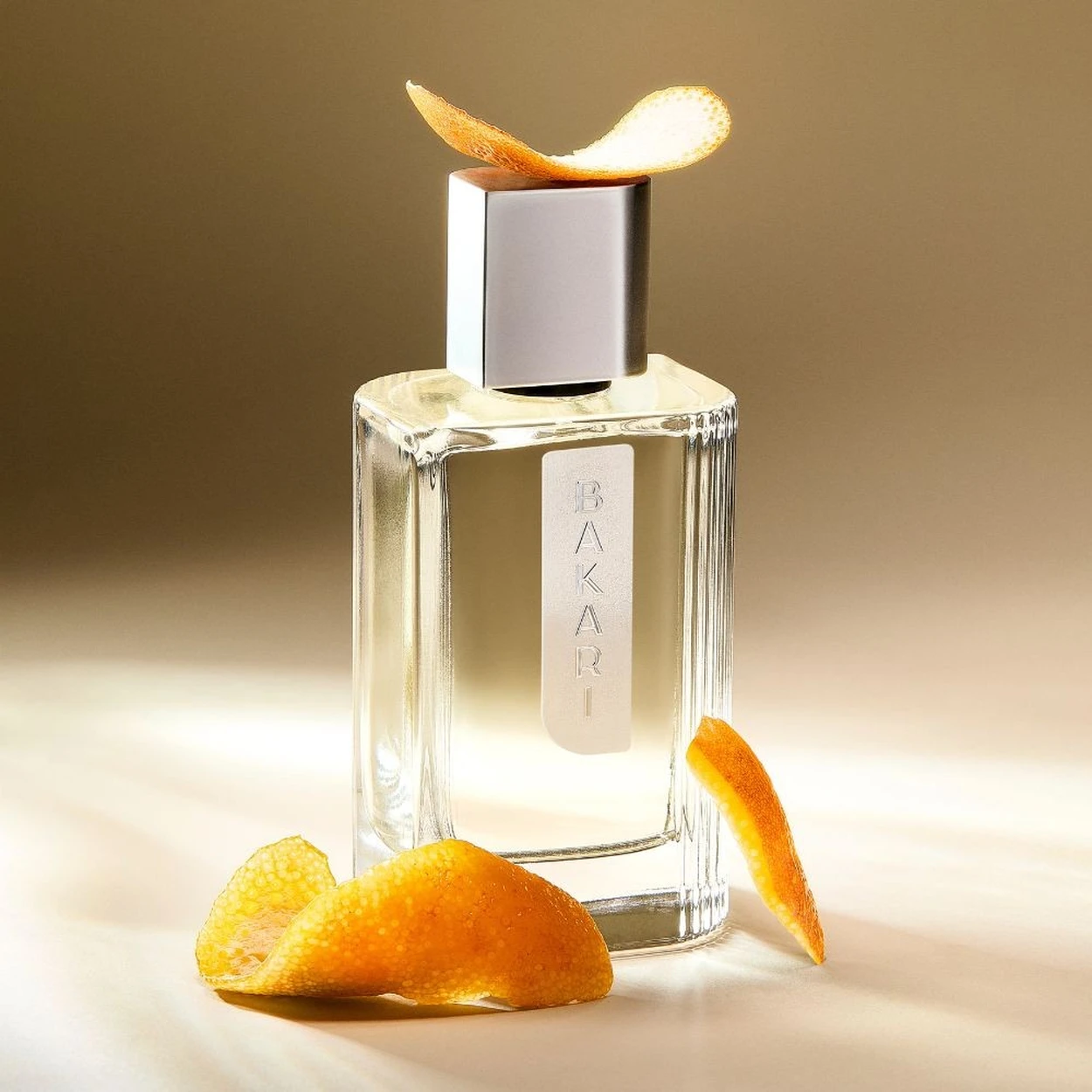 Frasco de perfume transparente com tampa prateada e casca de laranja decorativa.