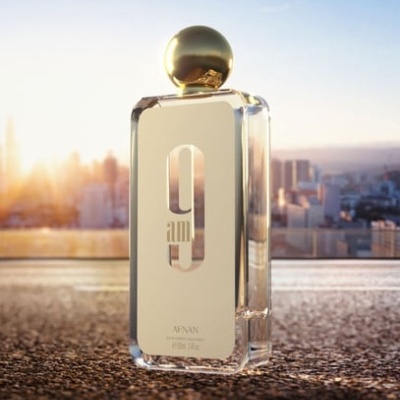Frasco de perfume dourado com tampa esférica numa superfície urbana ao pôr do sol