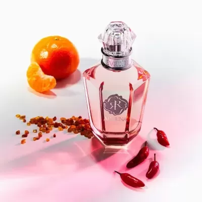 Frasco de perfume de vidro transparente com líquido cor de rosa junto a pimenta vermelha, grãos âmbar e tangerina descascada