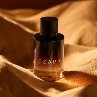 Frasco de perfume OZARA em vidro gradiente castanho sobre tecido dourado.