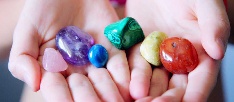 Mãos segurando seis pedras polidas coloridas