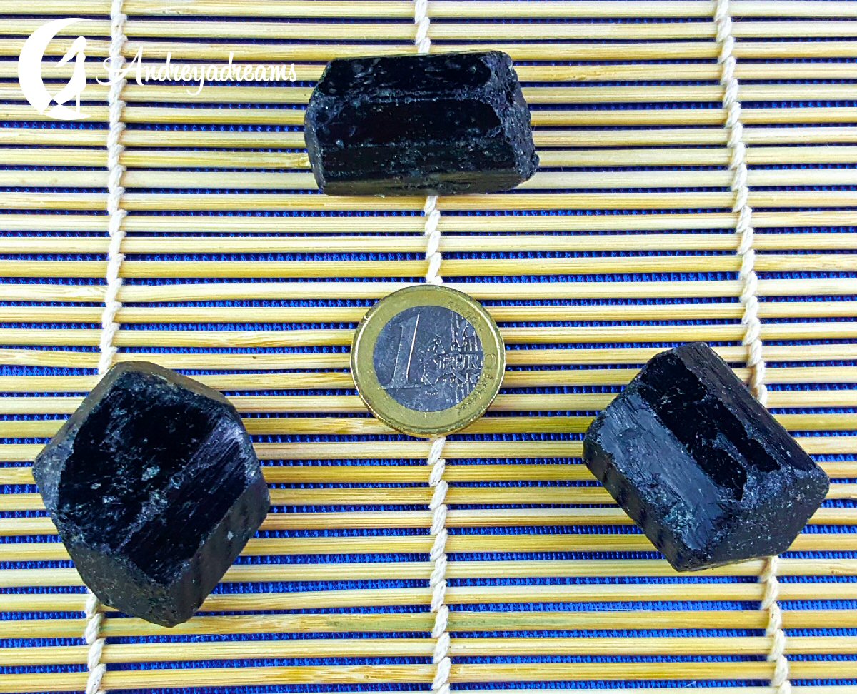 Turmalina Negra 3cm Três minerais pretos ao redor de uma moeda de 1 euro sobre uma esteira de bambu