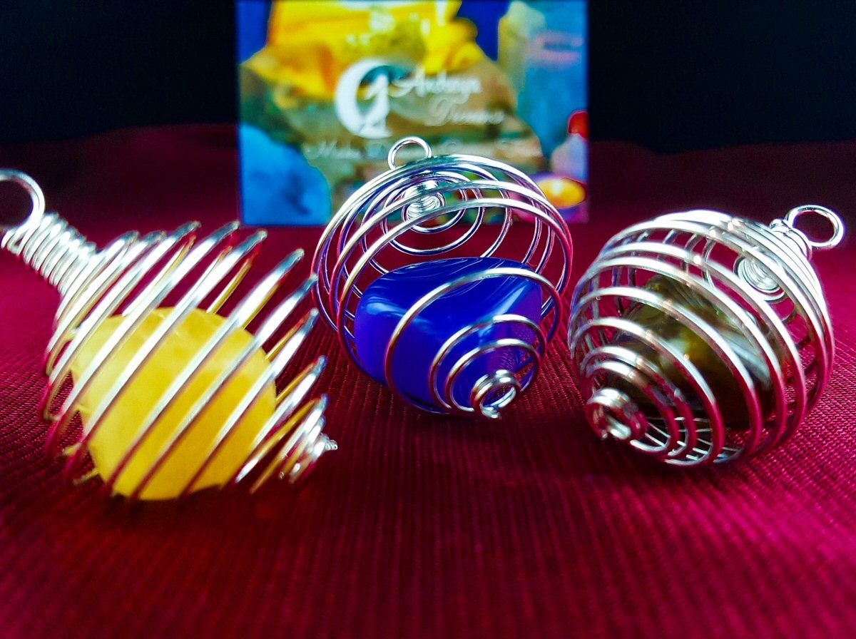 Pendente Espiral Gaiola para Pedras Três esferas coloridas em suportes metálicos em espiral sobre superfície vermelha.