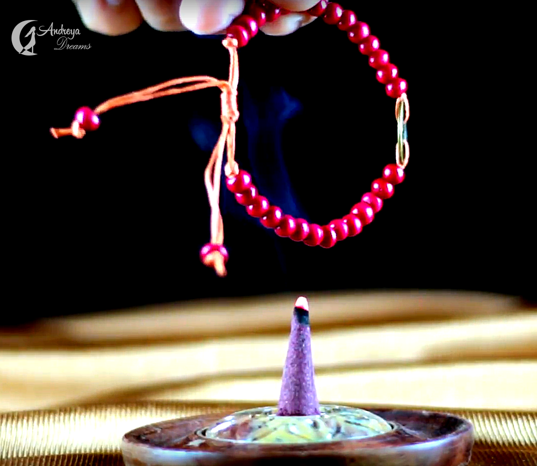 Limpeza Energética de Objetos com Incenso Pulseira vermelha com incenso cone roxo aceso numa base redonda