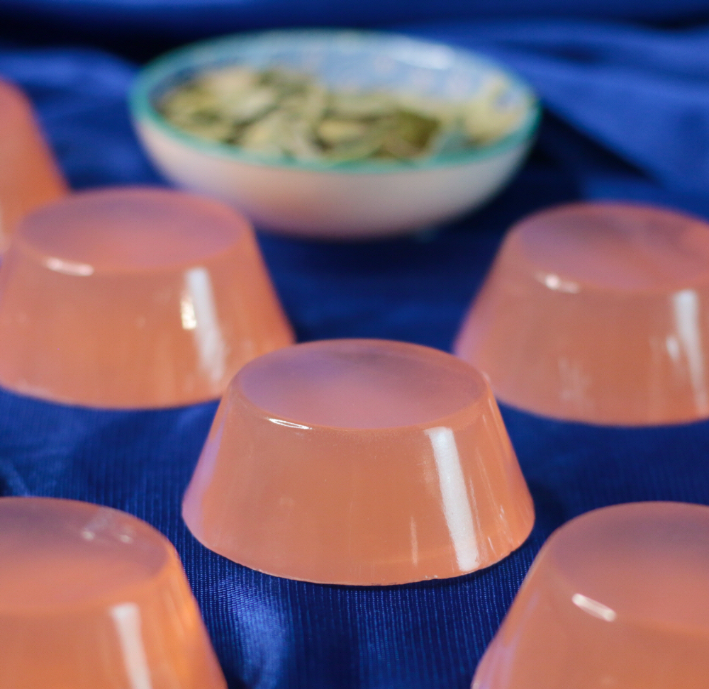 Sabonete de Boldo Gelatinas cor de rosa translúcidas sobre tecido azul com tigela de sementes ao fundo
