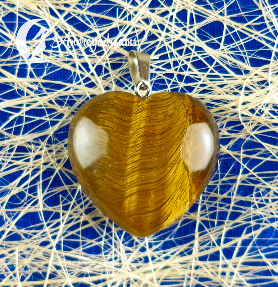 Pendente 💛 Coração Olho de Tigre Pendente em forma de coração amarelo com encaixe metálico sobre fundo azul com linhas brancas