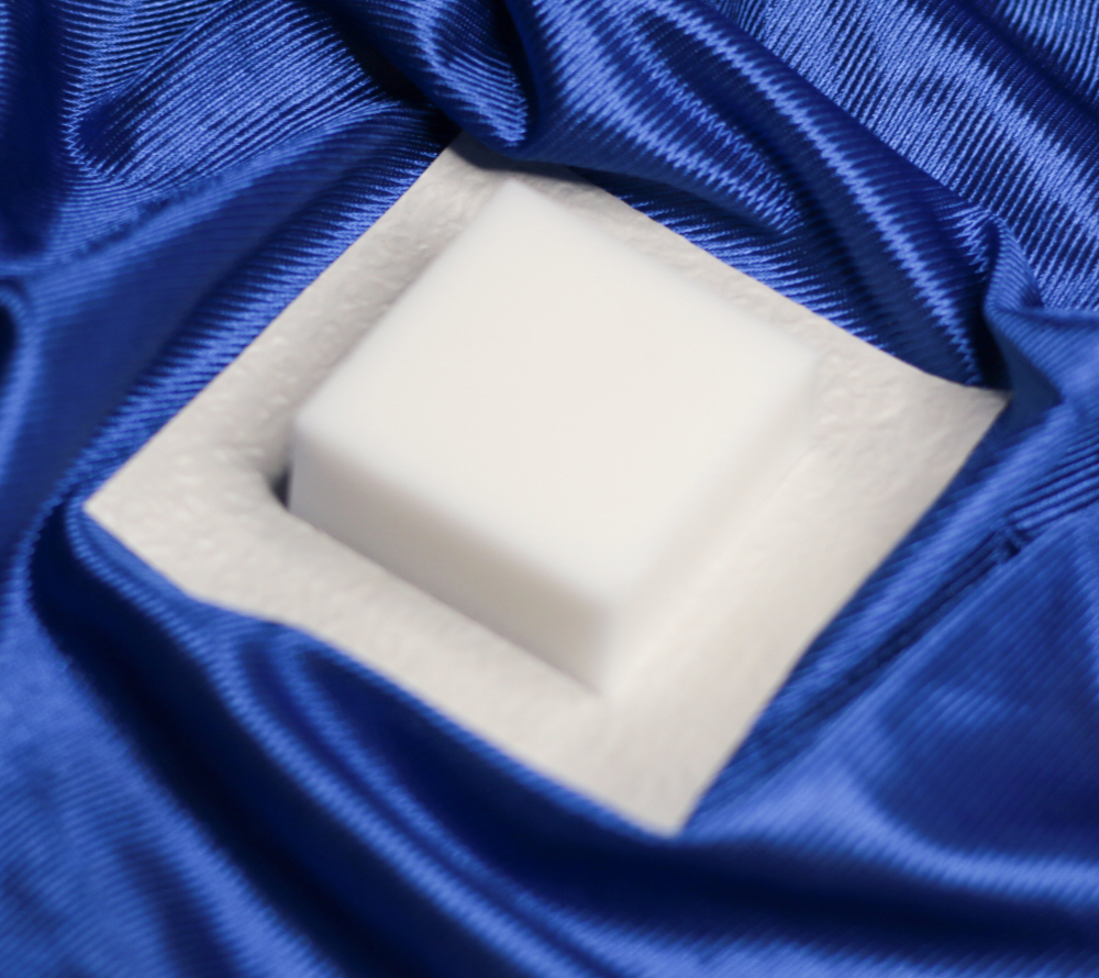 Sabonete de Cânfora Sabonete quadrado branco em embalagem branca sobre tecido azul acetinado