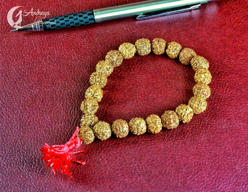 Pulseira de contas marrons com franja vermelha ao lado de caneta sobre superfície vermelha