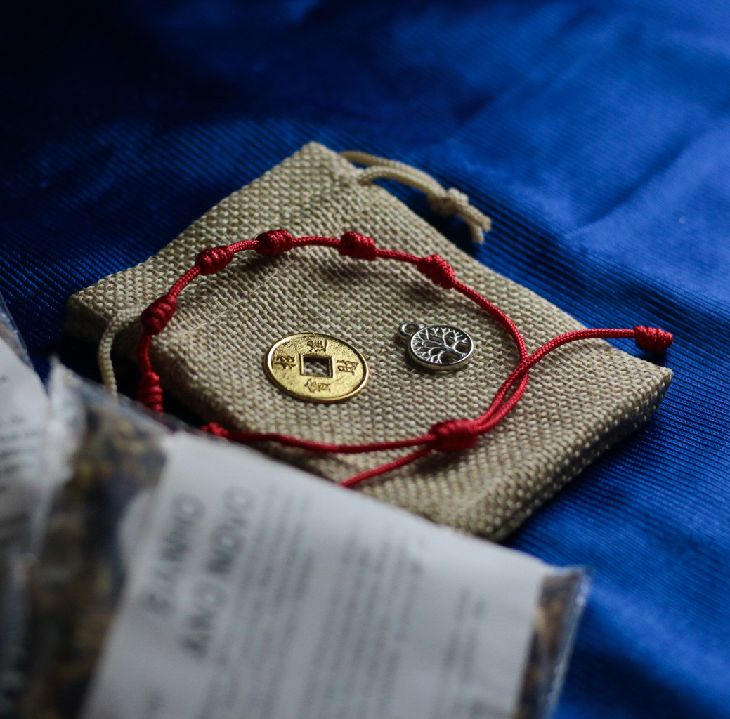 Kit Ano Novo Pulseira fio vermelho, moedas dourada e prateada num saco de pano sobre tecido azul