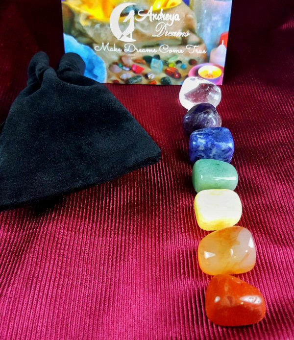 Kit Pedras dos 7 Chakras Conjunto de sete pedras coloridas e saco preto sobre tecido vermelho